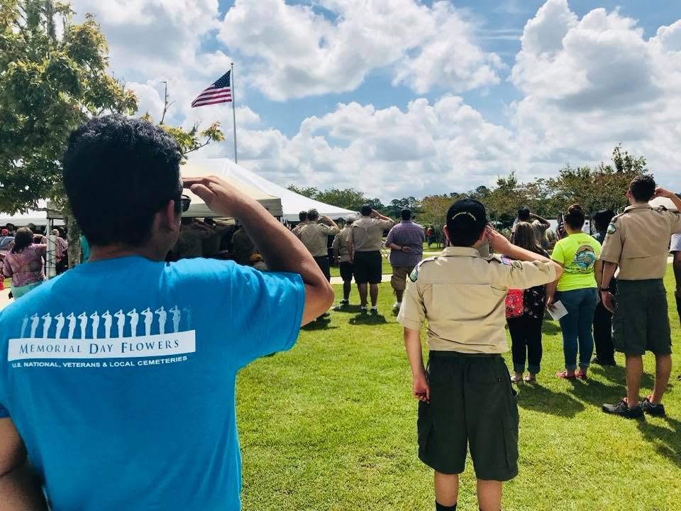 Volunteers in Memorial Day Flowers shirts saluting the flag at a veterans cemetery ceremony